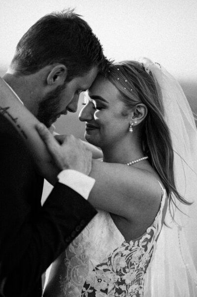 Bride and groom in an intimate embrace, touching foreheads and gleaming about their special day