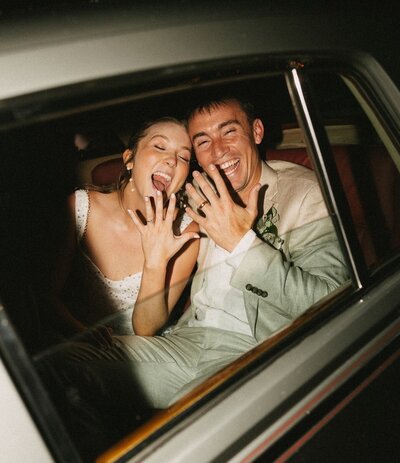 An image from a Wilmington wedding photographer of newlyweds smiling in the back of a car showing off their rings
