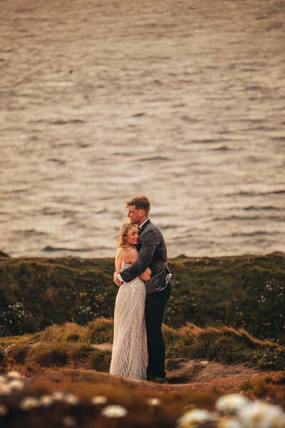 newly-married couple embrace by the ocean