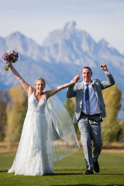 ust married couple celebrates with arms raised at Jackson Hole Golf and Tennis Club wedding, with the Grand Tetons towering behind them.