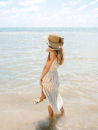 Kilee in a striped dress and straw hat standing in the ocean