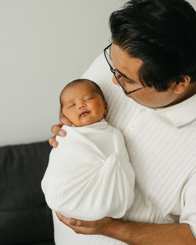 Bright, natural light photo of a baby girl being held by her dad.