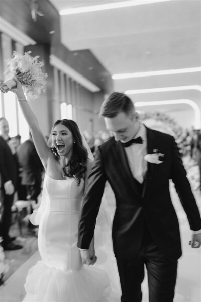 Black and white photo of bride and groom walking down the aisle holding hands