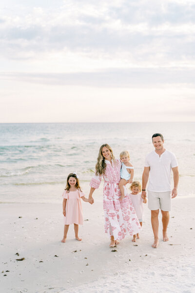 Family of five holding hands and walking on the beach with the ocean in the background