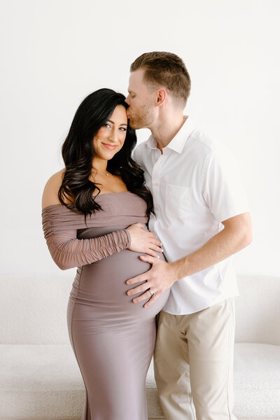 Expecting mom smiling at camera while husband kisses her forehead during Indianapolis studio maternity photos
