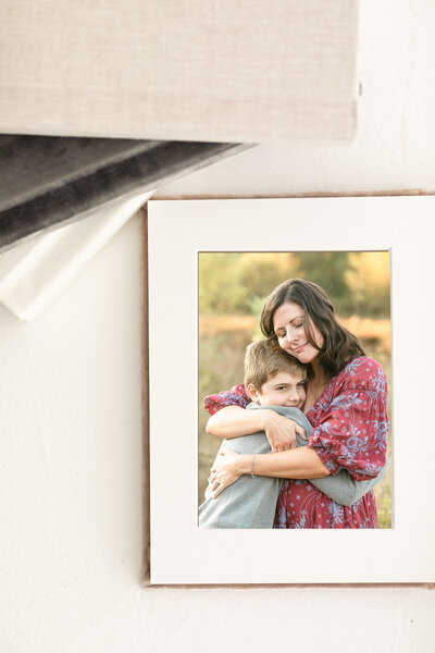 Photograph of mom in burgundy and blue floral dress hugging her 10 year old son who's wearing a grey sweater. Outdoor family photos in Oregon.