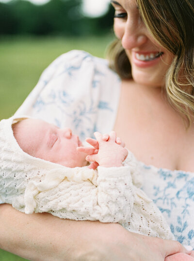 Mother holds newborn baby daughter in a cream, knit outfit as baby criss-crosses her fingers