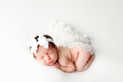 Newborn girl photo lying on tummy with big white bow covered with white lace. Fresno Clovis Newborn Photographer