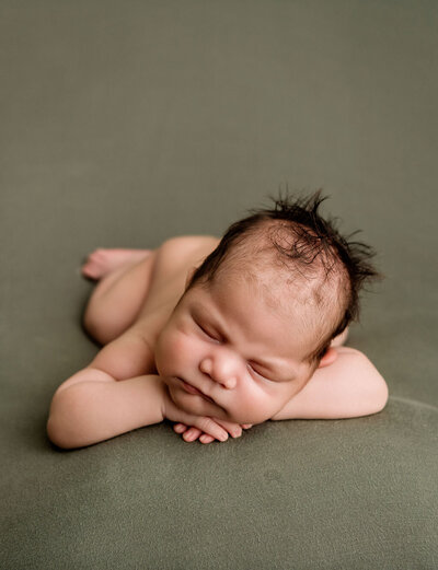 Professional newborn photography by Stamford CT photographer featuring sleeping baby in classic head-in-hands pose on sage green backdrop
