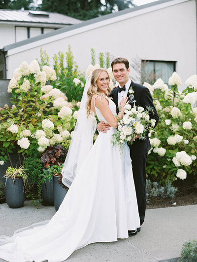 Seattle wedding photographers capture bride and groom pose for a classic portrait with white and green florals behind them
