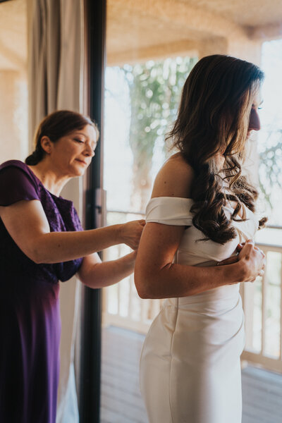 Mother of the bride buttons up bride's wedding dress before wedding ceremony by California elopement photographer Kasey Mantiply