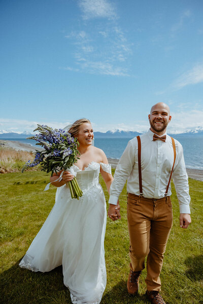 bride and groom holding hands walking along the water