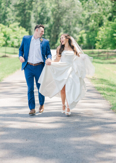 Bride and groom running down a road while bride is holding up her dress smiling at husband