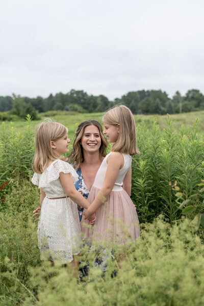 Mom smiling at two young daughters in a field