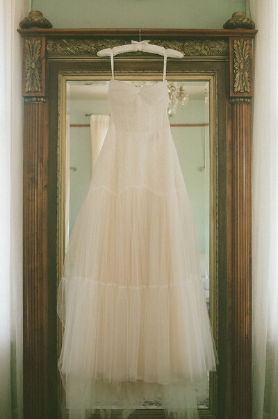 Tiered strapless tulle bridesmaid dress hanging in front of an ornate gold mirror