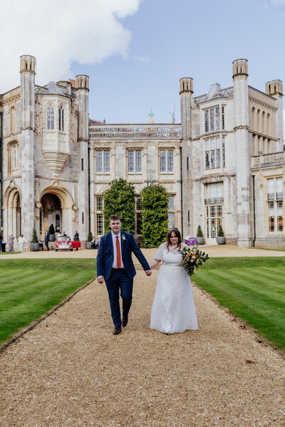 Bride and groom hold hands and walk infront of Highcliffe Castle