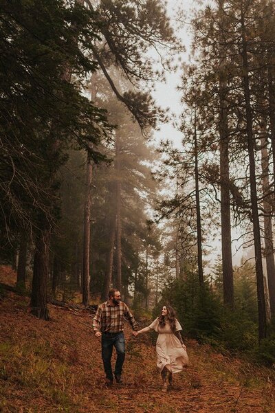 A couple holding hands and walking through the woods in the mountains.