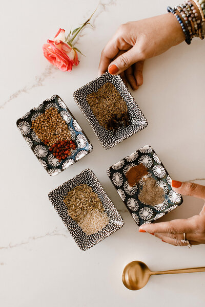 Four black and white dishes with powdered seasonings and herbs