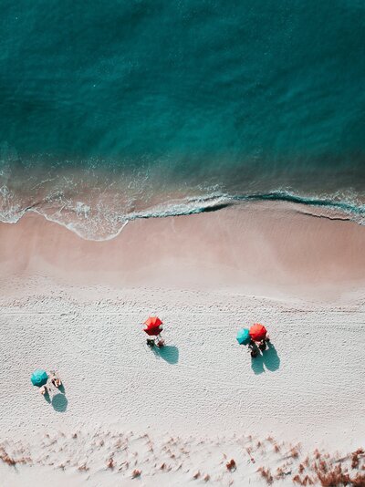 arial view of a white sand beach showing turquoise water and brightly colored beach umbrellas