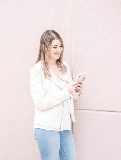 girl looking at her phone in front of a pink wall