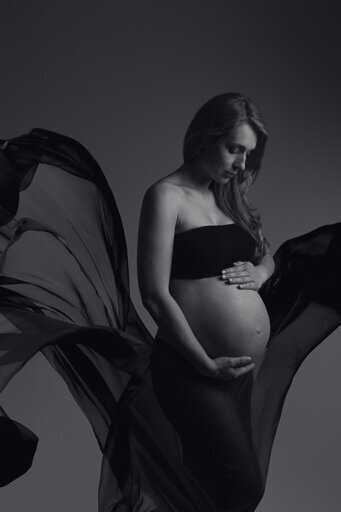 Maternity portrait of a woman with black flying fabric.