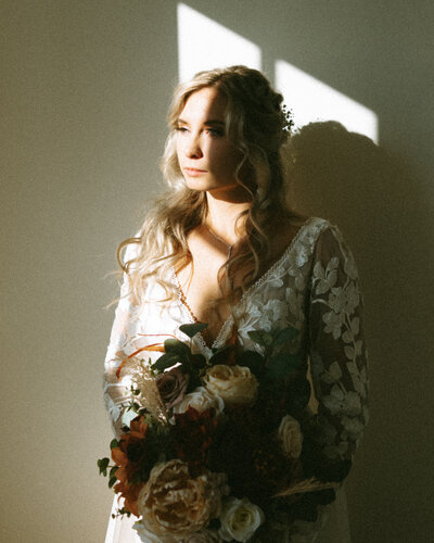 Blonde bride with a lacy long sleeve wedding dress holding bouquet