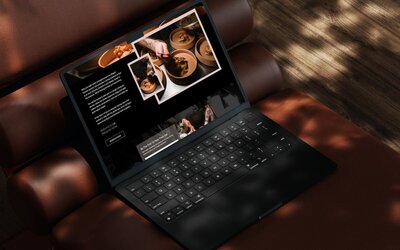 Black laptop on a brown leather seat showing a fine dining premium restaurant website with plated food photos and a tattooed chef preparing dishes.