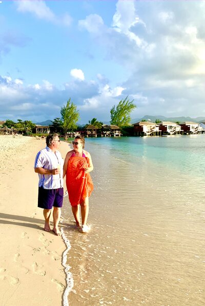 Man and woman holding hands walking along St. Lucia beach with champagne at sunset
