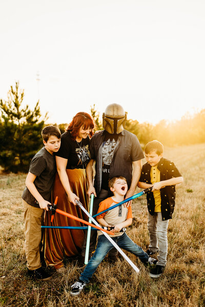 Allison with her husband and 3 boys with their lightsabers laughing