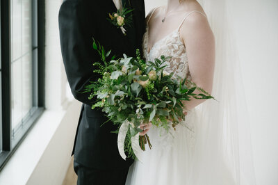 Newlyweds embracing in front of the expansive windows and exposed beams of The Arbor Loft’s loft-style interior.