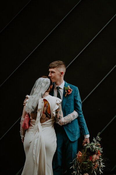A Tattooed bride and groom outside an industrial wedding venue. 