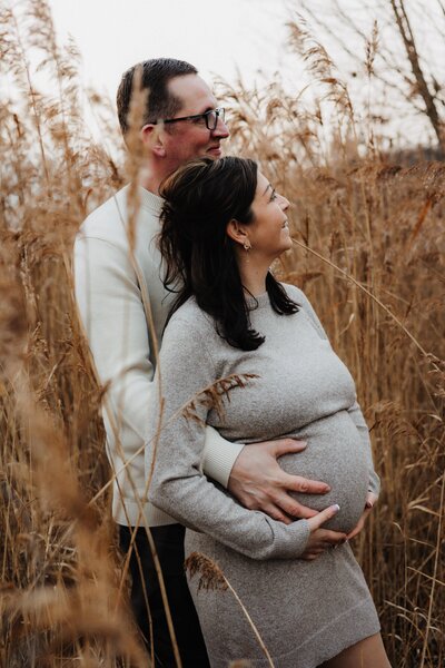 Mann und Frau stehen zwischen Schilf, Mann hält den Babybauch der Frau