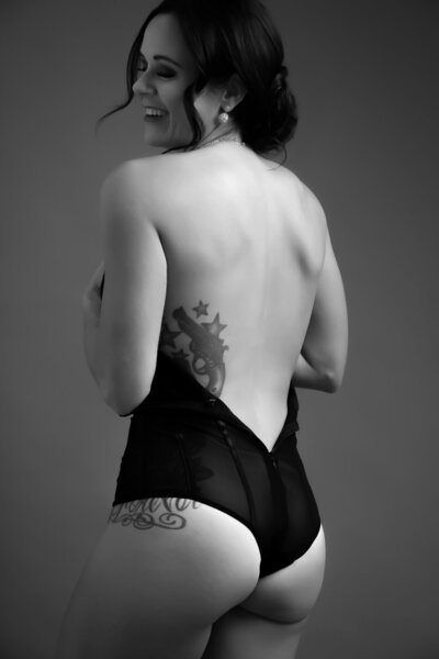 Women with hair up wearing a black bodysuit open on the back showing a tattoo