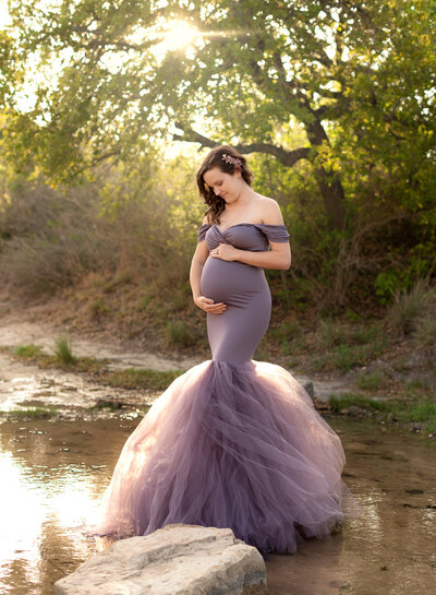 pregnant woman standing in a creek wearing a purple mermaid maternity dress with tulle