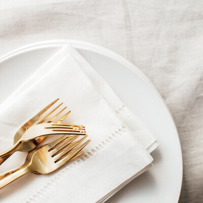 Gold forks rest on a white linen napkin atop stacked white plates.