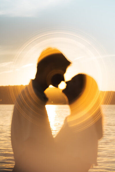 A silhouette of a bride and groom during golden hour with a lake backdrop