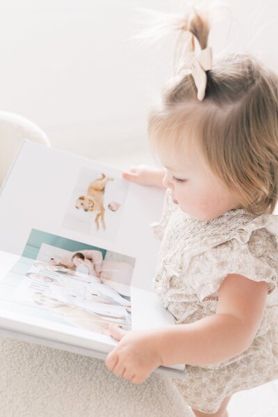 A little girl is looking at a photo book wiht images from her newborn session in charlotte north carolina