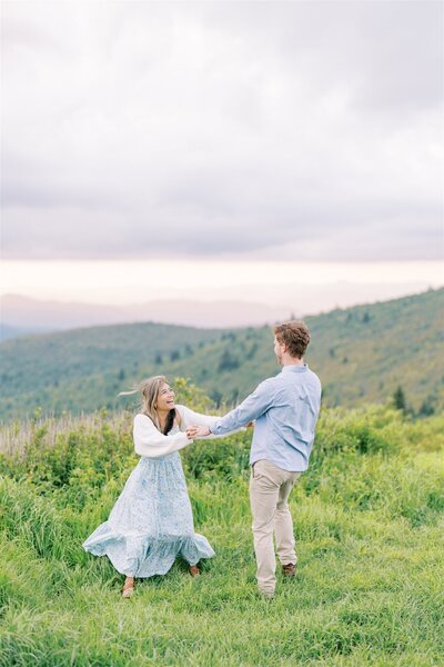 Candid couple frolics in feild surrounded by the mountains of NC