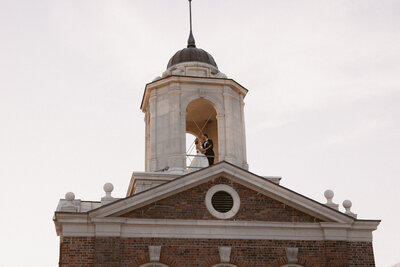 Bride and groom stand inside the open tower of a historic brick building at sunset.