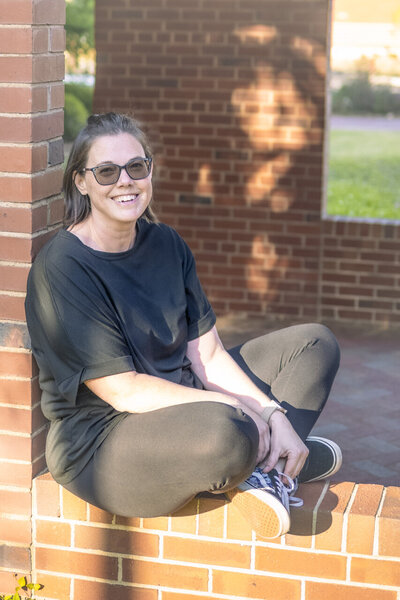 Birth and lifestyle newborn photographer in Tifton Georgia: self portrait of Sarah smiling at the camera, sitting cross-legged on brick wall