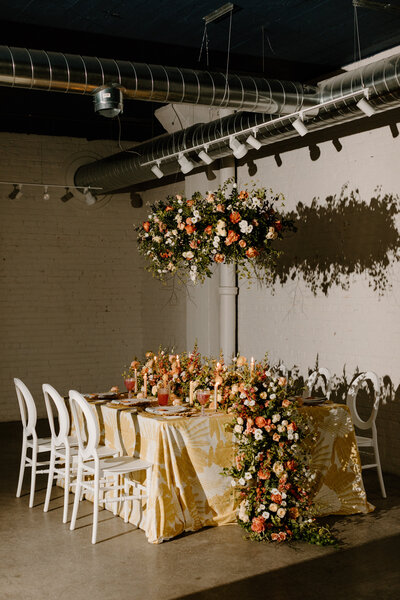 A small wedding reception table with a long floral arrangement in the middle 