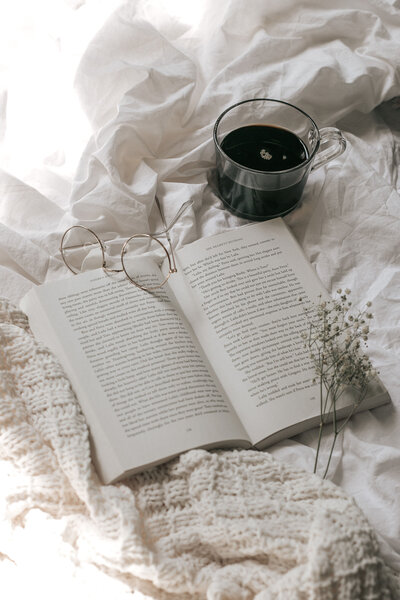 Image of book on bed with flowers glasses and coffee