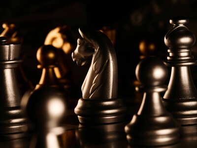 A close-up of a chessboard featuring metallic gold and silver chess pieces, with a knight piece in sharp focus under dramatic lighting.