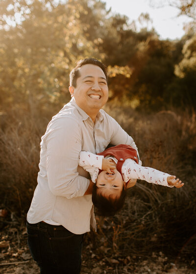 Dad holding his daughter upside down while laughing during a playful family photo session on a nature trail in Pasadena, California. 