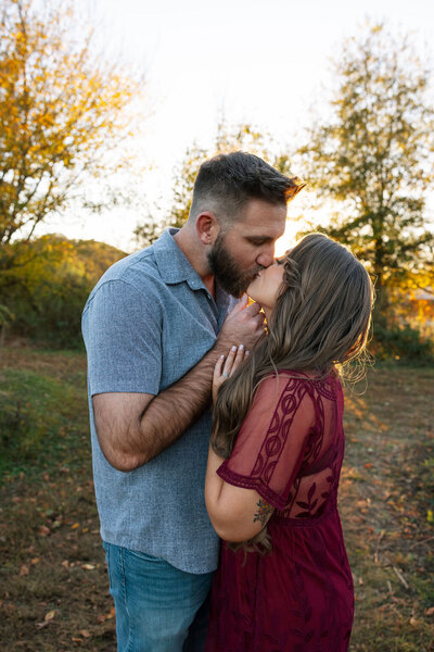 engagement photo by Photographer Knoxville TN of couple kissing in a field with the smoky mountains in the distance during the fall 