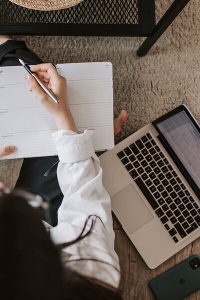 Person taking notes beside laptop, representing Pinterest marketing best practices for business profile success