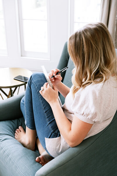 Girl sitting on chair wearing jeans and white shirt taking notes on a notepad