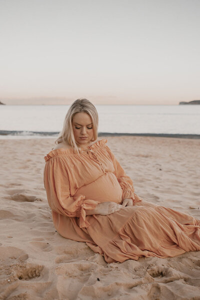 Pregnant lady sitting on sand with orange dress on
