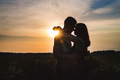 silhouette of a couple woman with arms around the neck of her fiance with sunburst and flare behind them