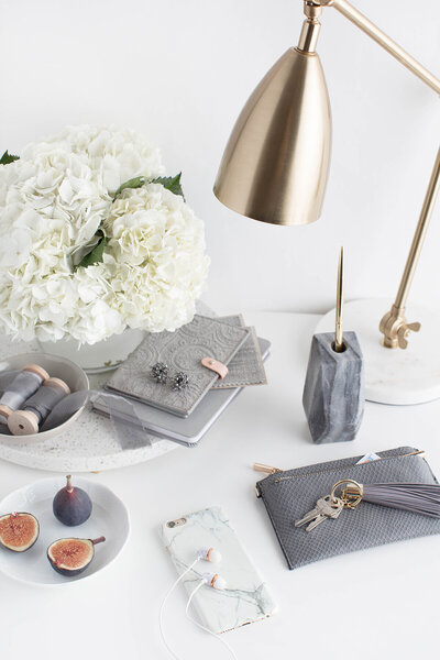 A desktop with white flowers, a gold lamp and grey stationer
